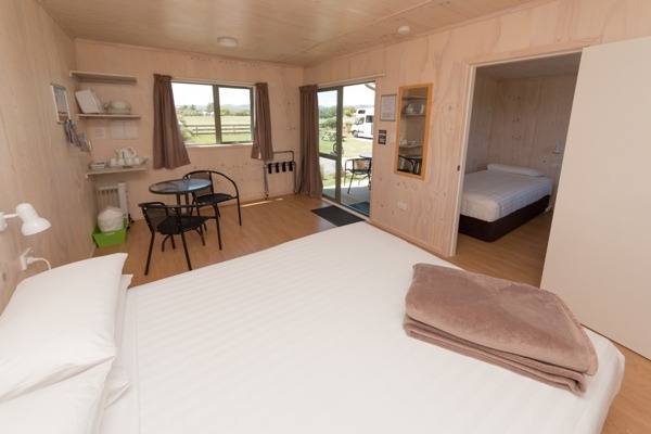 Photo of a two room cabin with a queen bed in the main room and two singles in the second room.