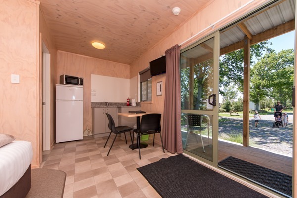 Photo of a studio motel unit at Martinborough Holiday Park showing the kitchen area and view of trees out of the ranchslider.